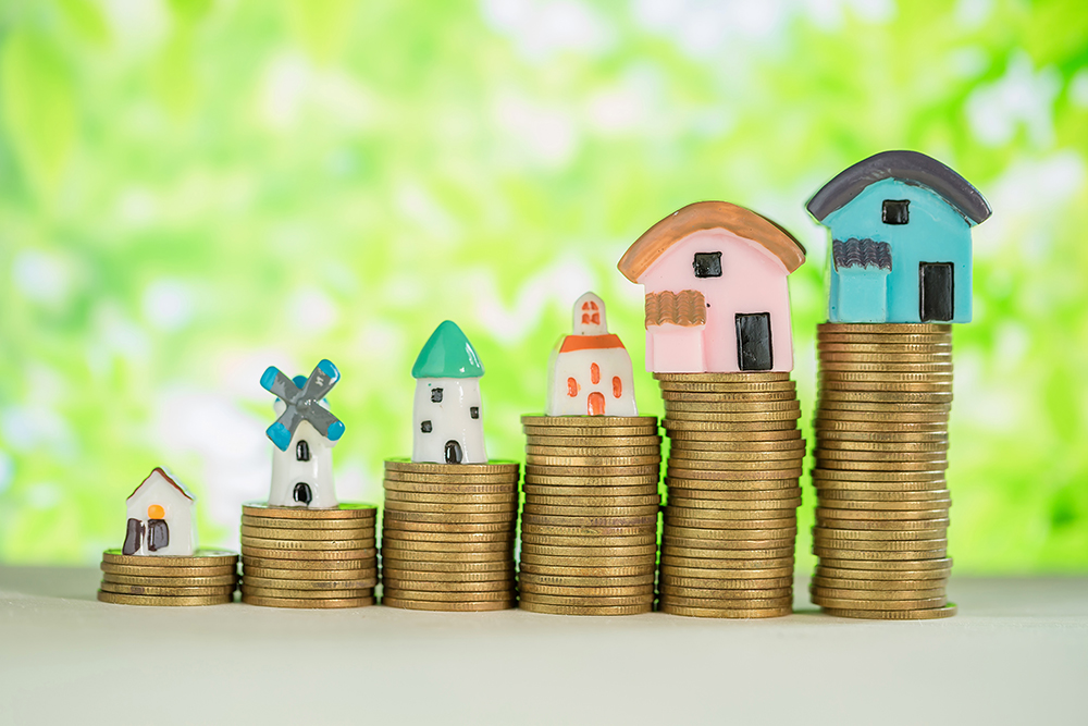Investment property concept. Mini house on stack of coins with green blur background.